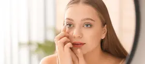 A woman is looking in the mirror and holding her eye with her hand.