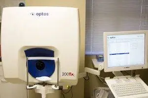 A medical imaging device with a monitor displaying a blue line, set up in a room with a window covered by blinds.