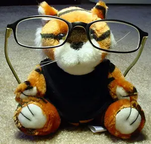 A close up of a plush tiger wearing glasses and a black shirt sitting on a carpeted floor.