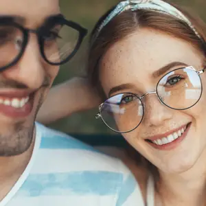 A man and woman smile and look at each other outside in a park