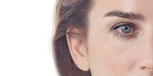 A close up of a woman's face with blue eyes and brown hair, slightly looking to the side, on a white background