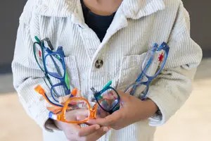 A child holds a variety of glasses in their hands, including one with a red logo.