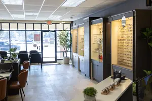 A room with an entrance door and chairs, a table with potted plants, a glass door with a potted plant, and a lamp hanging from the ceiling.