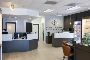 A modern office space with a reception desk, computer monitors, and potted plants, featuring a logo for Allied Vision Plainsboro.