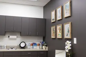 A bathroom with gray cabinets, a sink, a mirror, and a few picture frames on the wall.