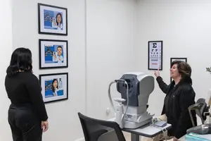Two women standing inside a room with a vision testing machine, one woman is pointing at it