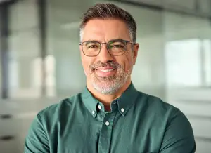 Smiling man with gray hair wearing glasses and a green shirt in an office