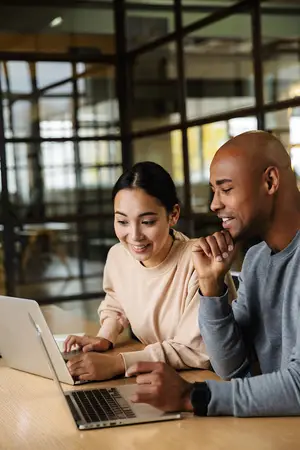 A man and a woman sitting at a table, smiling and looking at a laptop