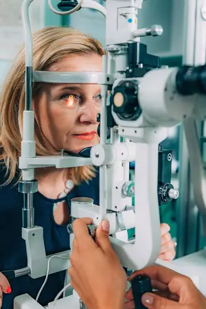 A woman is having her eyes examined by an optometrist using a slit lamp.