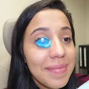 A woman with a blue patch on her right eye is smiling and posing for a picture.