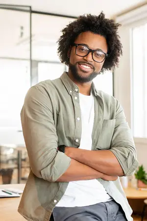 A man with curly hair and glasses is smiling and posing for a photo in an office room