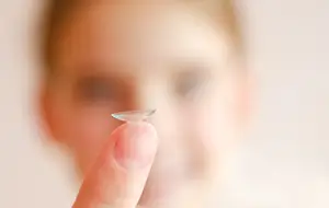 A person holds a clear contact lens on their fingertip.