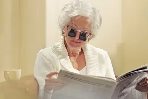 Elderly woman reading a newspaper while wearing sunglasses
