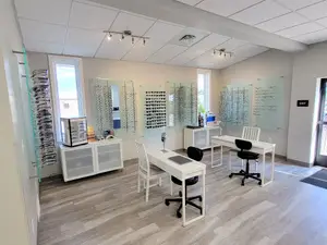 Interior of an optical shop with desks, chairs, and glasses on display on the wall.