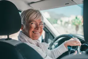 Happy older woman wearing glasses driving a car in a parking lot