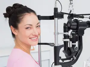 A woman is smiling while standing in front of an ophthalmoscope machine