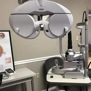 An eye examination machine from the brand NIDEX is on a table next to a wall with a picture frame.