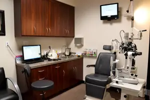An interior of an ophthalmology clinic with a monitor, an eye examination machine, and a sink on the countertop.