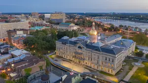 A top-down view of a city skyline featuring a prominent government building with a golden dome at dusk, surrounded by other buildings, trees, and a river