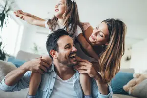 A man in a blue shirt carrying a young girl on his shoulders while a woman smiles next to him