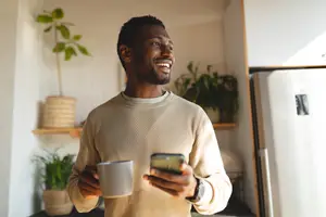 Man smiling while holding a cup and a cell phone