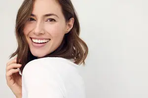 Portrait of a woman smiling with a white shirt and her hand on her shoulder
