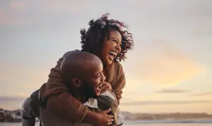 A woman holding a man on the beach at sunset