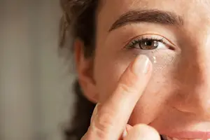 Close up of a woman's face with a contact lens on her fingertip.