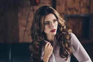 Portrait of a woman with glasses and red lipstick posing for a photo in a cozy room