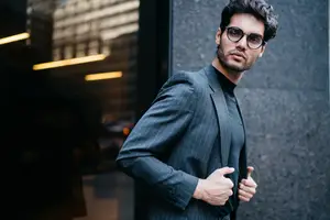 A man wearing a suit and glasses is standing in front of a building.