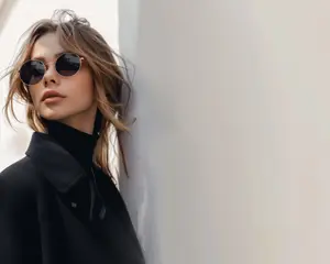 Woman wearing sunglasses and a black coat leaning against a wall