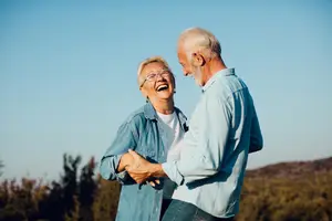 An older couple dancing outside in front of trees and mountains