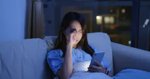 Woman sitting on a couch with her eyes closed and holding a phone