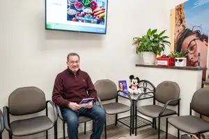 A man is sitting in a chair in a waiting room, reading a book and smiling.