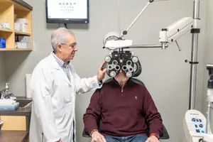 An elderly man getting his eyes checked by an older man in a white coat in an optometrist's office.