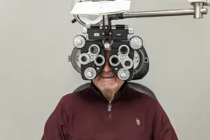 Man in a burgundy sweater undergoing an eye examination with a professional autorefractor