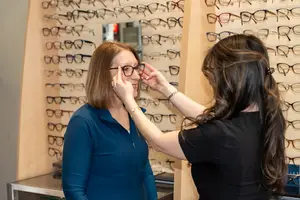 A woman trying on glasses in an optical store with a salesperson assisting her