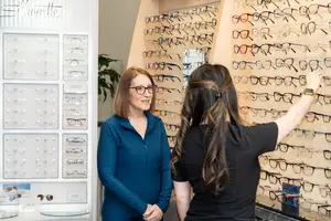 A woman in glasses is looking at a display of frames while standing next to another woman in a blue shirt.