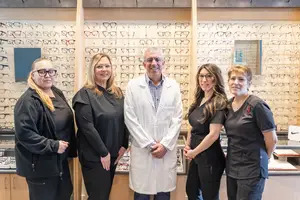 Five people standing in front of a wall of glasses in an optometrist office