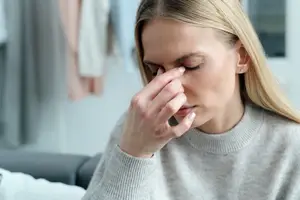 A woman sitting on a couch and holding her nose while closing her eyes.