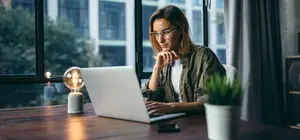 Woman sitting at a table with a laptop and a lamp.