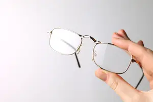 A hand holding a pair of glasses with clear lenses and gold frames
