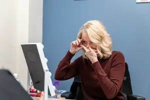 A blonde woman is sitting in a chair and adjusting her glasses with her hands