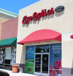 Eye Optics Optometry Center store front with a red awning and sign with a car parked in front.
