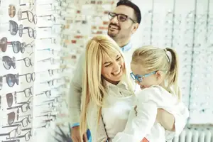 A family is smiling while looking at a display of sunglasses in a store.