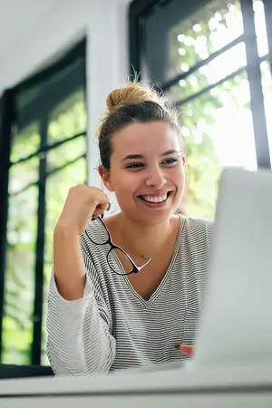 woman smiling and holding glasses at a computer