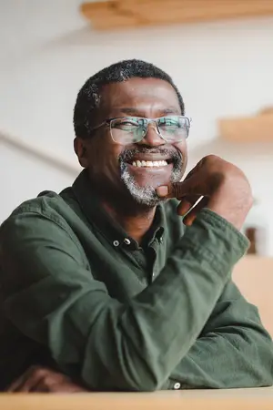 A smiling man wearing glasses sits at a wooden table.