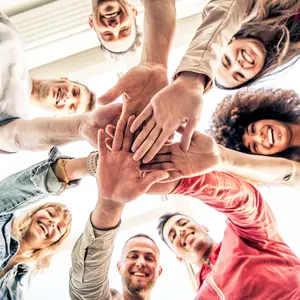 Group of friends with their hands on top of each other, smiling and looking forward.