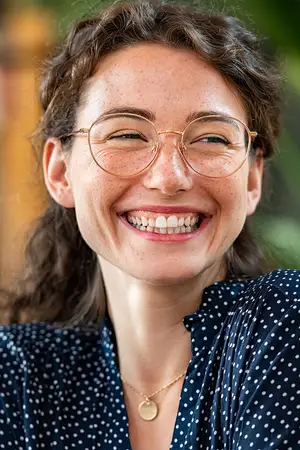 Woman with curly hair wearing a blue polka dot shirt and glasses smiling at the camera