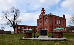 A red building with a clock tower and cannons on a lawn.